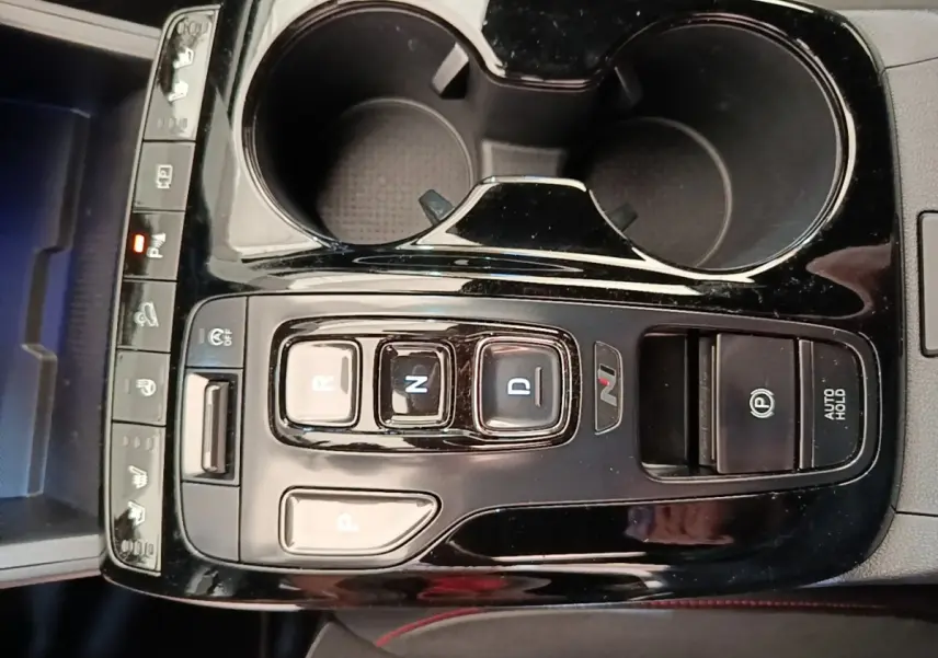 Vue rapprochée de la console centrale noire avec commandes de boîte auto et deux porte-gobelets du Hyundai Tucson rouge.
