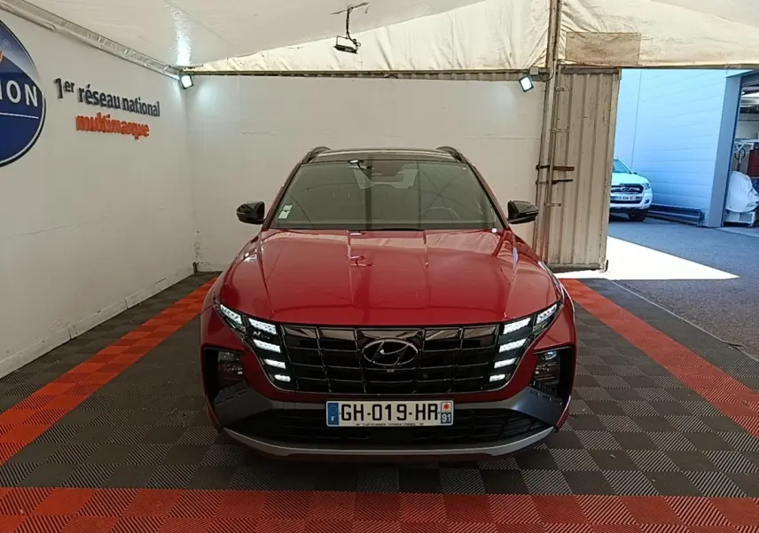 Vue frontale d'un Hyundai Tucson rouge 2022 avec calandre noire et feux LED distinctifs allumés.