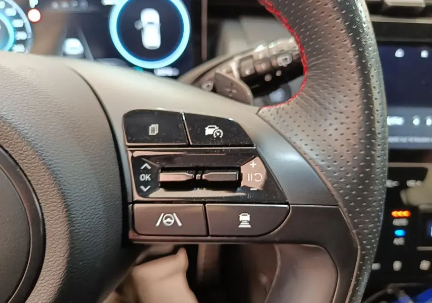 Gros plan sur les commandes multifonctions à gauche du volant cuir perforé rouge du Hyundai Tucson rouge 2022.