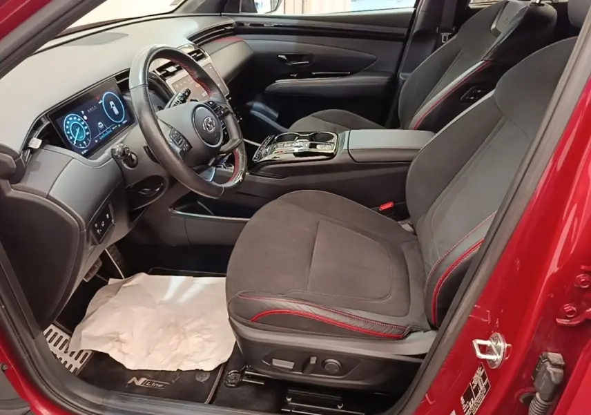 Vue intérieure côté conducteur du Hyundai Tucson rouge, avec sièges noirs à surpiqûres rouges et tableau de bord digital.