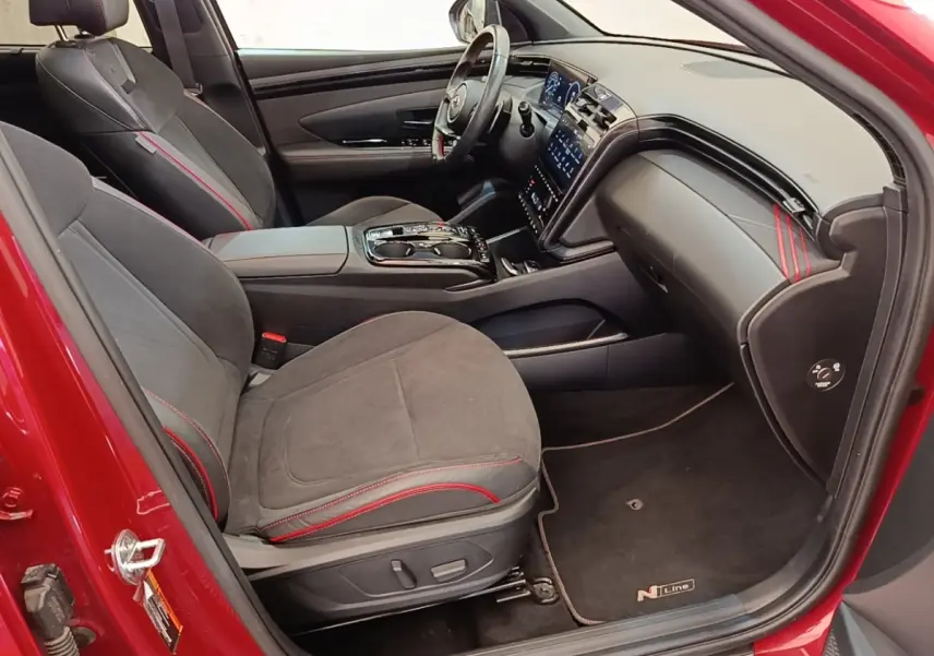Vue intérieure côté conducteur du Hyundai Tucson rouge 2022, sièges noirs avec surpiqûres rouges et tableau de bord moderne.