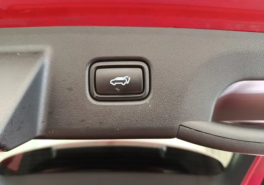 Bouton d'ouverture électrique du coffre sur le hayon intérieur d'un Hyundai Tucson rouge, vue rapprochée.