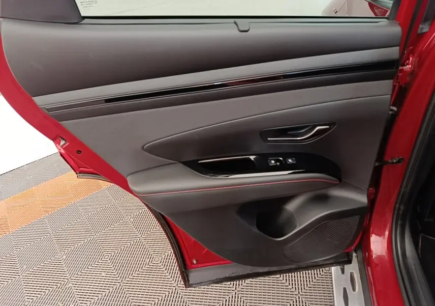 Vue rapprochée de la porte arrière gauche rouge du Hyundai Tucson 2022 avec garniture noire et surpiqûres rouges.