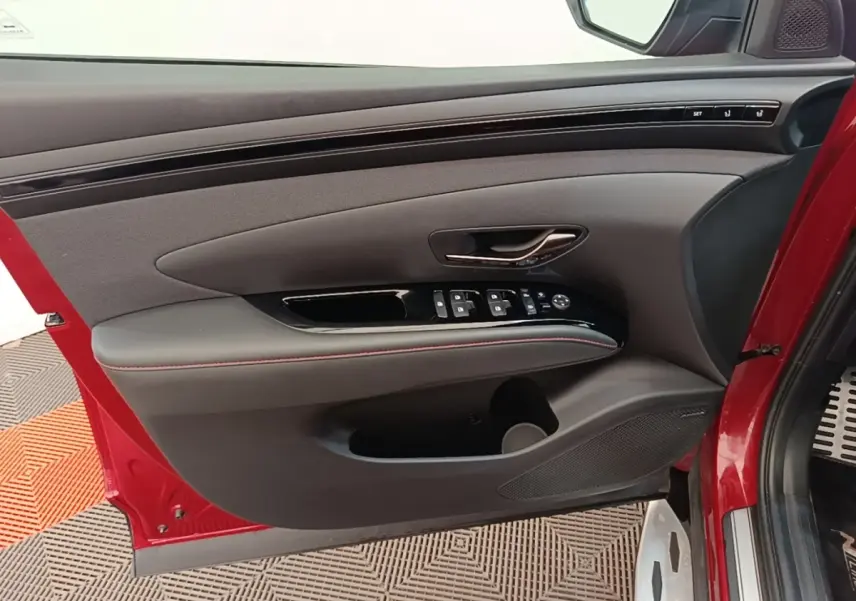 Vue intérieure de la porte avant gauche rouge du Hyundai Tucson 2022 avec commandes électriques et surpiqûres rouges.
