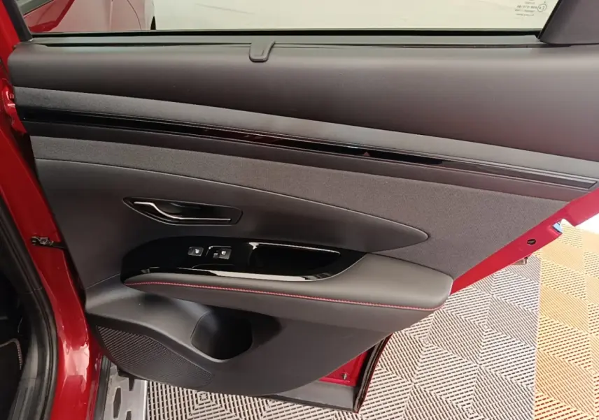 Vue intérieure de la porte arrière gauche rouge du Hyundai Tucson 2022 avec commandes de fenêtre et surpiqûres rouges.