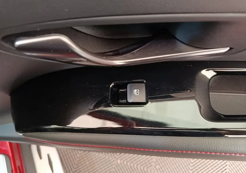 Détail de la commande de verrouillage électrique sur la porte intérieure noire avec surpiqûres rouges du Hyundai Tucson rouge.