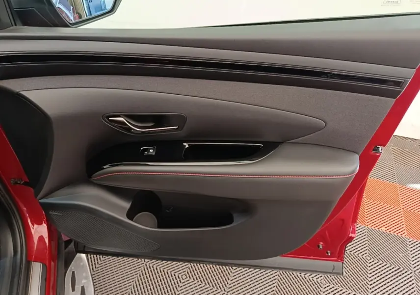 Intérieur côté gauche de porte rouge Hyundai Tucson 2022, avec garniture noire et surpiqûres rouges.