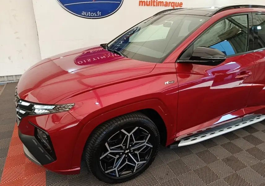 Vue 3/4 avant droit d'un Hyundai Tucson rouge N Line avec jantes noires et marchepieds argentés.