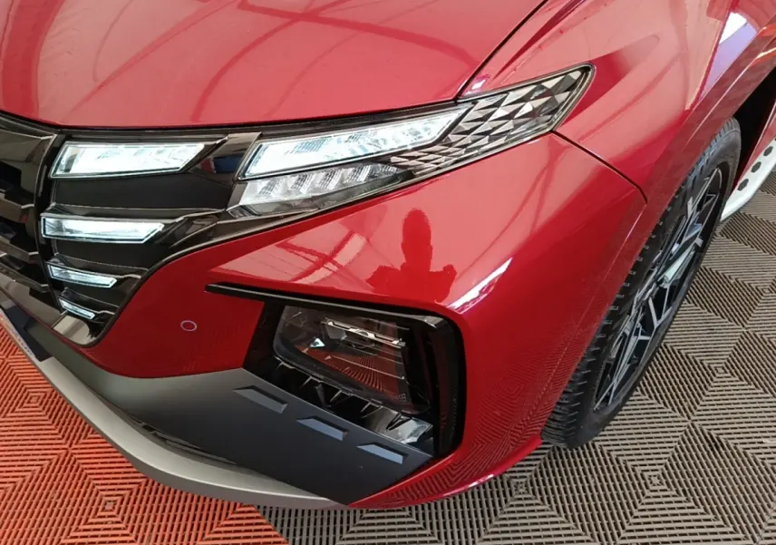 Gros plan sur l'avant droit rouge du Hyundai Tucson 2022, mettant en valeur les phares LED et la calandre noire brillante.