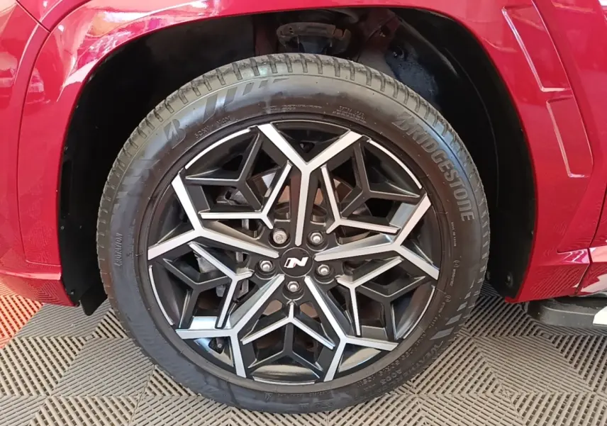 Gros plan sur la roue avant droite du Hyundai Tucson rouge, jante alliage noire et argentée au design géométrique N Line.