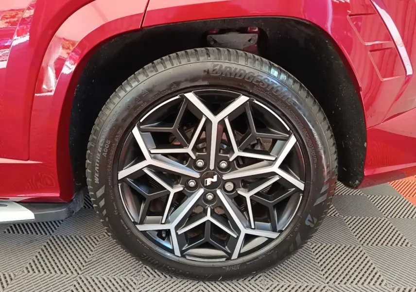 Gros plan sur la roue avant droite du Hyundai Tucson rouge 2022, mettant en valeur la jante noire et argentée au design géométrique.
