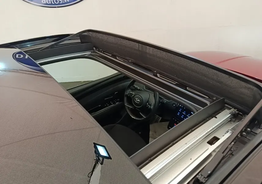 Vue plongeante sur l'intérieur via toit ouvrant du Hyundai Tucson rouge, montrant volant et écran tactile allumé.