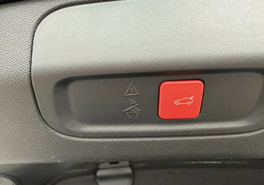 Gros plan sur le bouton rouge d'ouverture électrique du coffre dans l'habitacle d'une Peugeot 408 PHEV 225 GT.