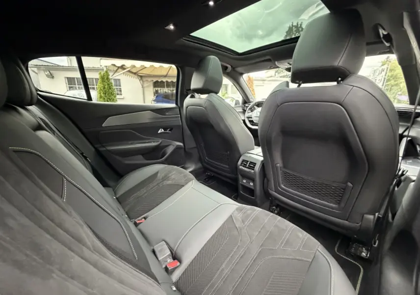 Intérieur arrière de la Peugeot 408 PHEV 225 GT 2023, sièges noirs, toit panoramique et tableau de bord visible en avant.