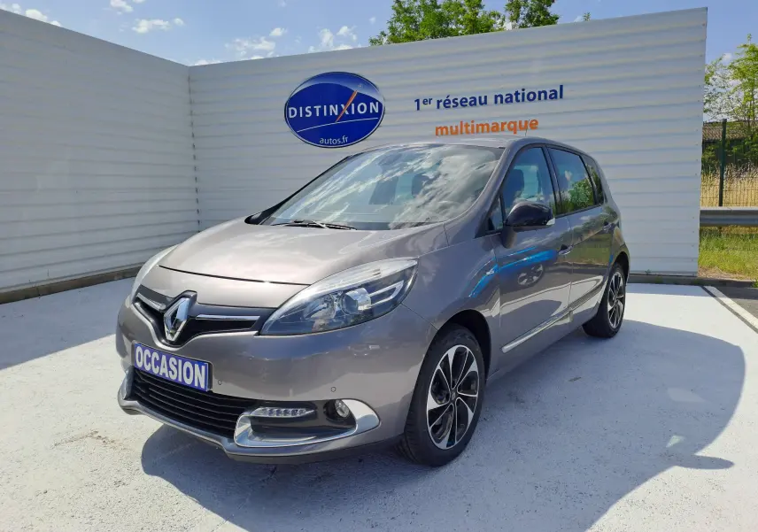 Renault Scenic III gris en 3/4 avant droit, avec jantes alliage noires et logo Renault bien visible sur calandre.