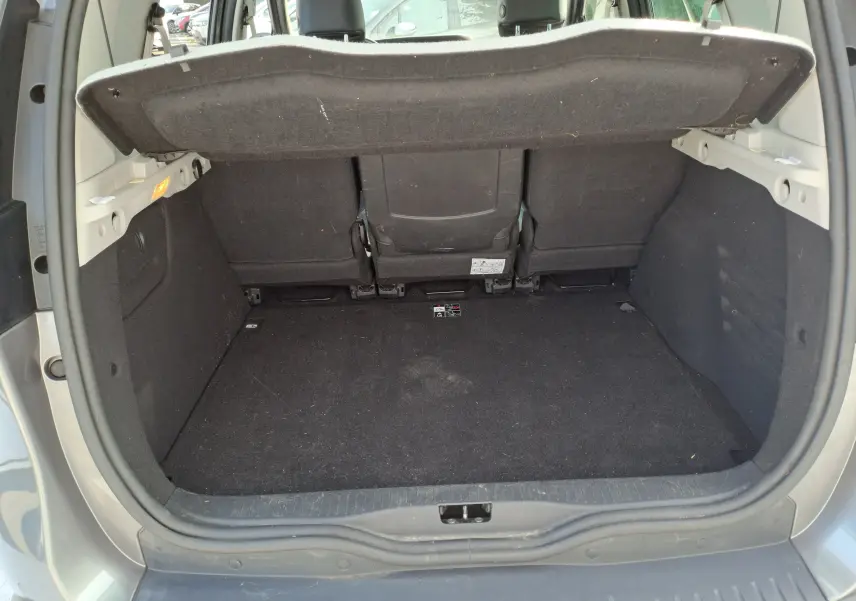 Coffre ouvert d'un Renault Scenic III gris, vue arrière montrant l'espace de chargement et la plage arrière relevée.