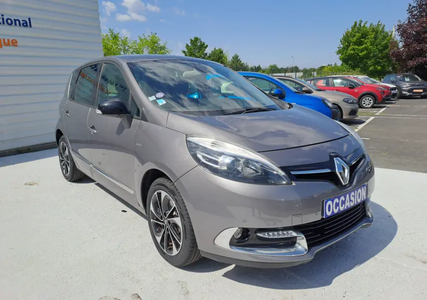 Renault Scenic III gris en 3/4 avant droit, avec jantes alliage et feux avant LED visibles sur parking extérieur.