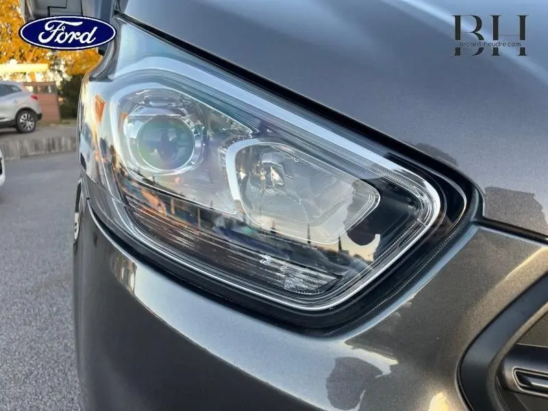 Gros plan sur le phare avant gauche du Ford Transit Custom gris Magnétic métallisé, soulignant ses lignes modernes.