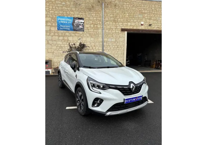 Renault Captur blanc en 3/4 avant droit, avec toit noir et détails noirs contrastants sur un parking extérieur.