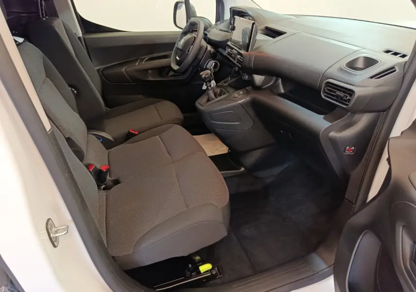 Intérieur du Peugeot Partner blanc vu côté passager, montrant les sièges avant et le tableau de bord moderne avec écran tactile.
