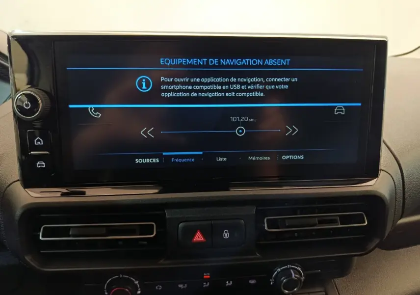 Vue rapprochée de l'écran multimédia et de la console centrale noire du Peugeot Partner blanc, affichant un message d'absence de navigation.