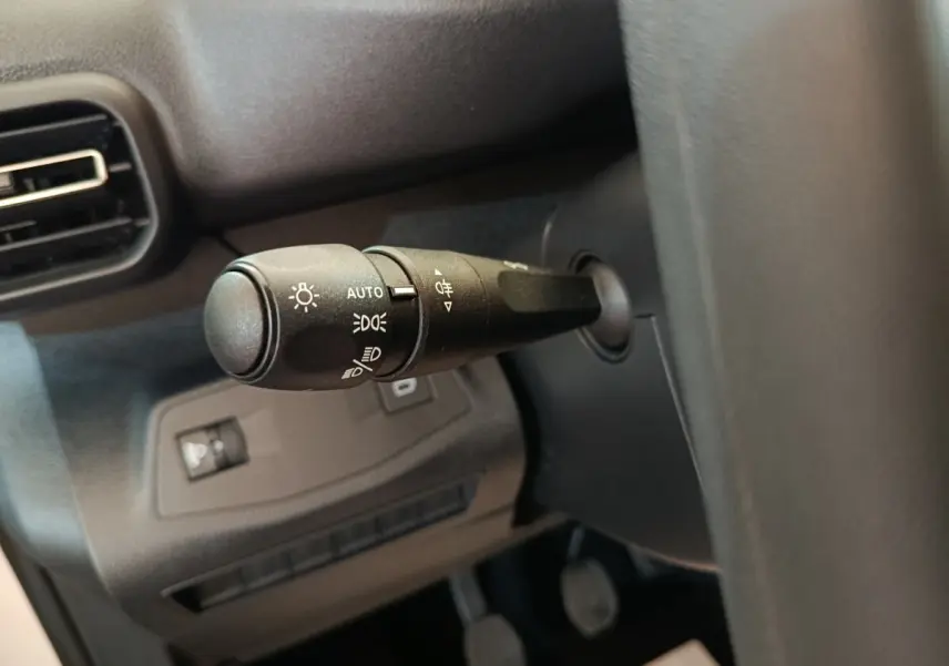 Gros plan sur le commodo des phares à gauche du volant dans l’habitacle sombre du Peugeot Partner blanc 2025.