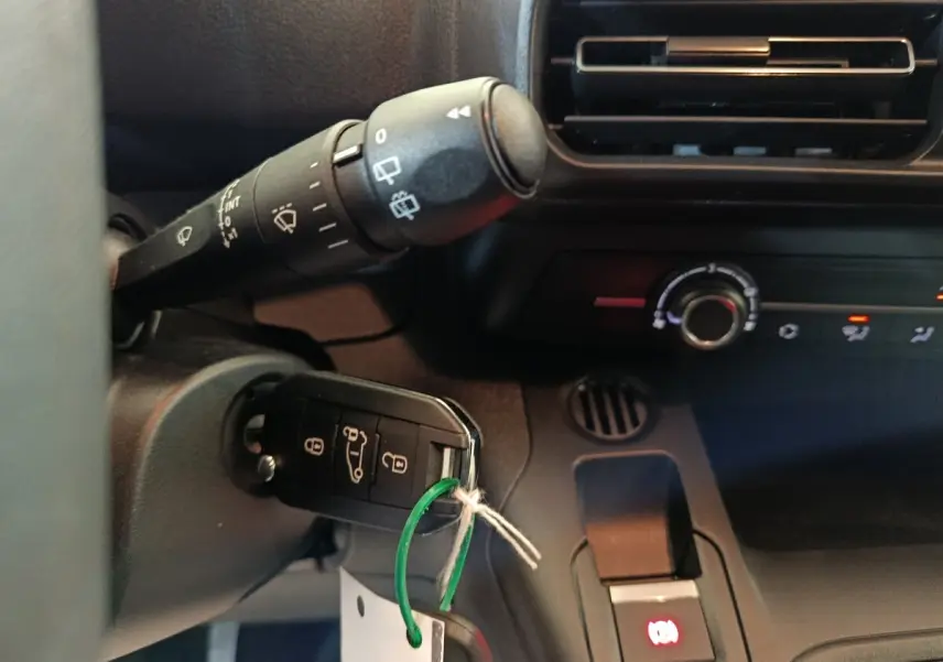 Gros plan intérieur sur la clé insérée dans le contact et la commande de climatisation du Peugeot Partner blanc 2025.
