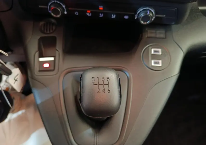 Le levier de vitesses manuel noir du Peugeot Partner 2025 vu de dessus, avec ports USB et commandes de climatisation.