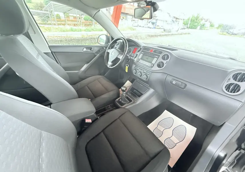 Vue intérieure côté conducteur du Volkswagen Tiguan noir 2007, montrant sièges tissu noirs et tableau de bord avec boîte manuelle.