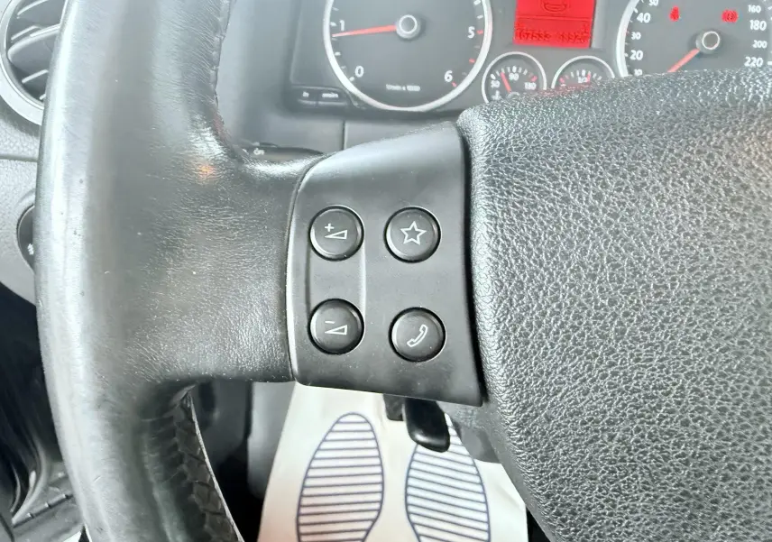 Gros plan sur le volant noir du Volkswagen Tiguan 2007, avec commandes audio et téléphone visibles à gauche.