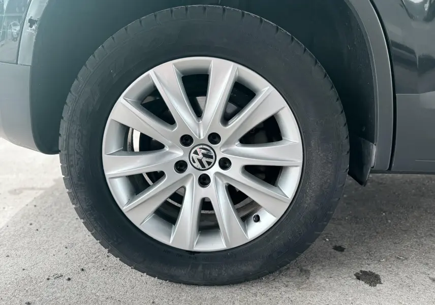 Gros plan sur la roue avant gauche avec jante argentée et logo Volkswagen sur un Volkswagen Tiguan noir.