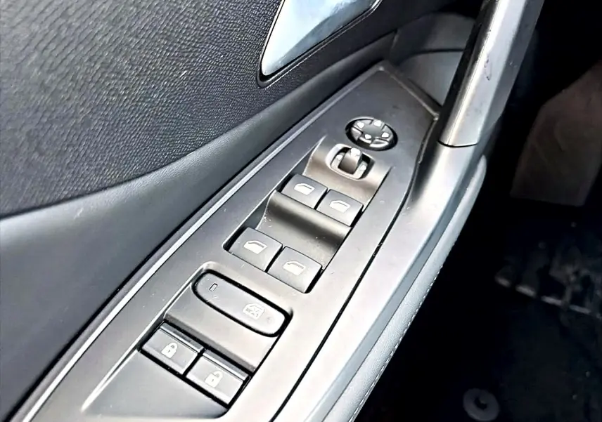 Gros plan sur les commandes des vitres et rétroviseurs côté gauche d’une Peugeot 408 noire, version Hybrid 145 allure 2025.