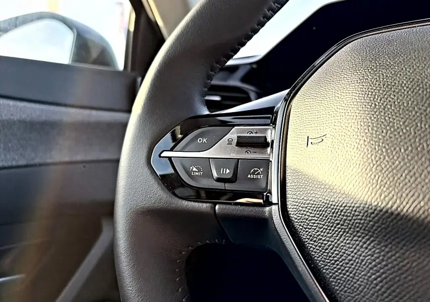 Gros plan sur le volant cuir noir de la Peugeot 408 Hybrid 145 allure, montrant les commandes multifonctions côté gauche.