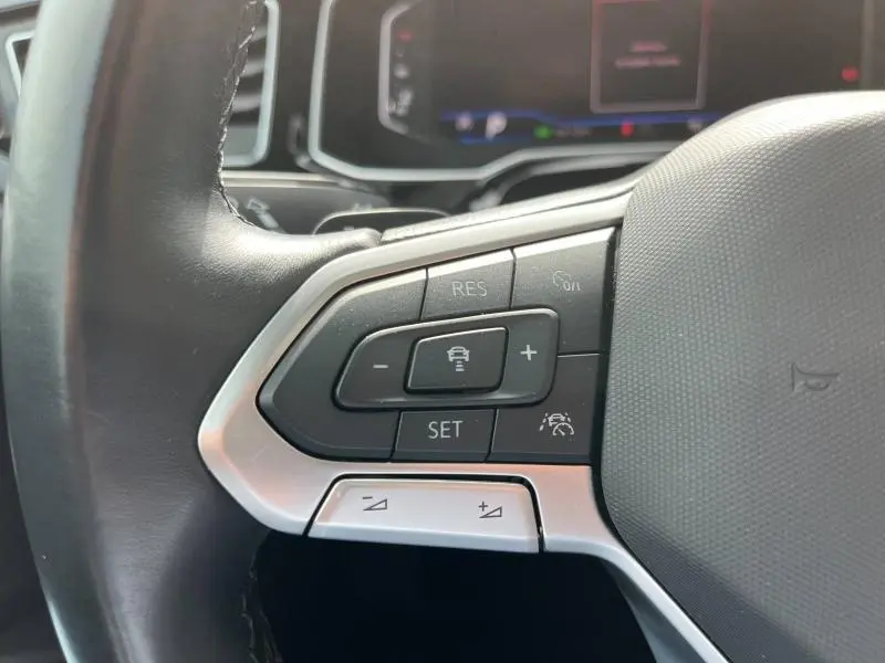 Gros plan sur les commandes multifonctions du volant cuir du Volkswagen Taigo 1.5 TSI R-Line 2023, avec boutons de régulateur de vitesse.