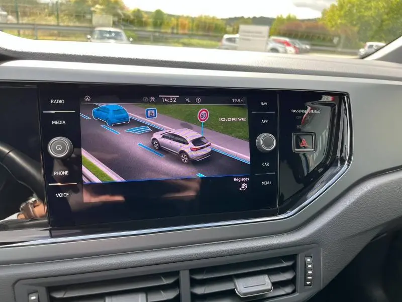 Écran tactile du tableau de bord montrant l'assistance IQ.DRIVE avec représentation d'une Volkswagen Taigo bleue en conduite.