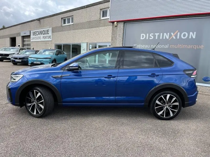 Profil latéral gauche d'un Volkswagen Taigo 1.5 TSI R-Line bleu récif métallisé avec jantes alliage et barres de toit noires.