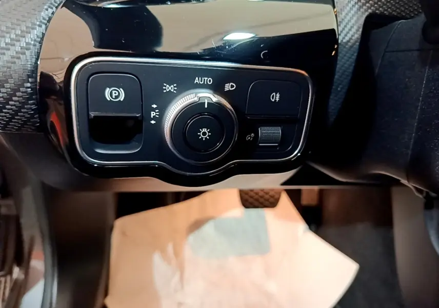 Gros plan sur le panneau de commande des phares et du frein à main électrique dans une Mercedes Classe A gris foncé.