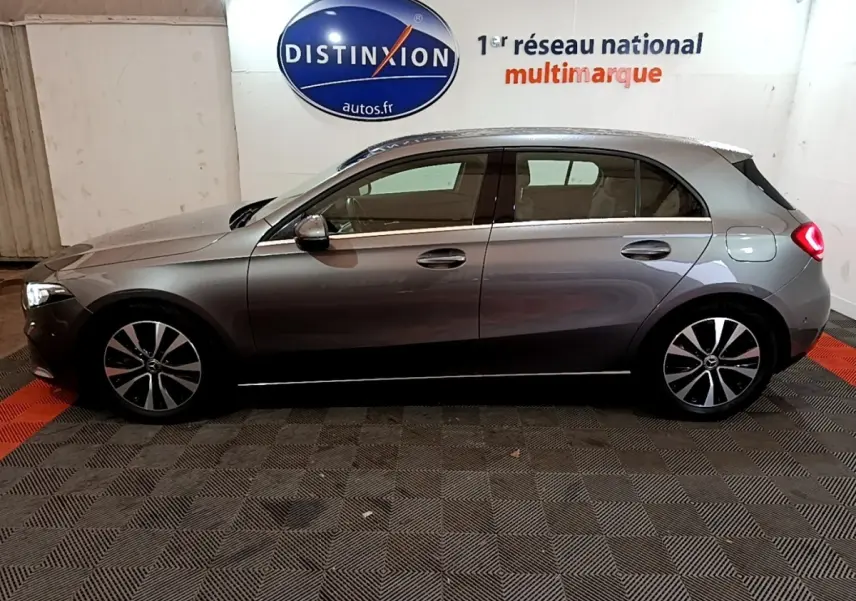 Vue de profil côté gauche d'une Mercedes Classe A 180 d Business Line gris foncé avec jantes alliage et feux arrière allumés.