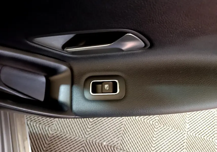 Détail du bouton de verrouillage électrique sur la porte intérieure noire d’une Mercedes Classe A gris foncé.