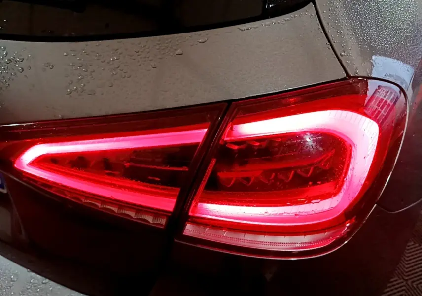 Gros plan sur le feu arrière droit allumé d’une Mercedes Classe A gris foncé sous la pluie.