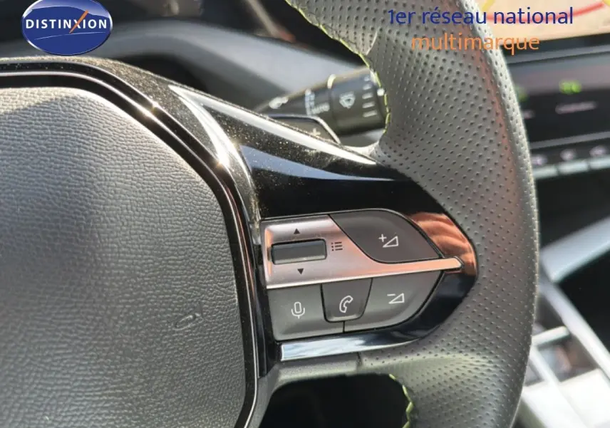 Gros plan sur les commandes multifonctions du volant en cuir perforé d'une Peugeot 408 gris selenium metal.