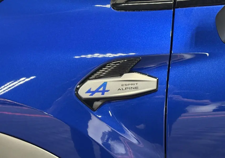 Gros plan sur l'aile avant gauche bleu Iron du Renault Symbioz avec badge Esprit Alpine bleu et noir brillant.
