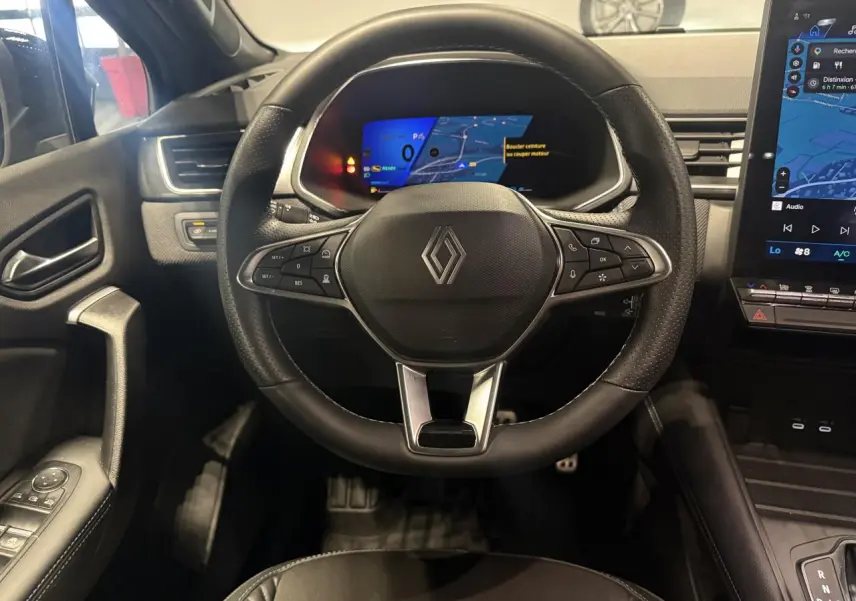 Vue intérieure centrée sur le volant noir de la Renault SYMBIOZ 2025 avec tableau de bord numérique et écran tactile latéral.