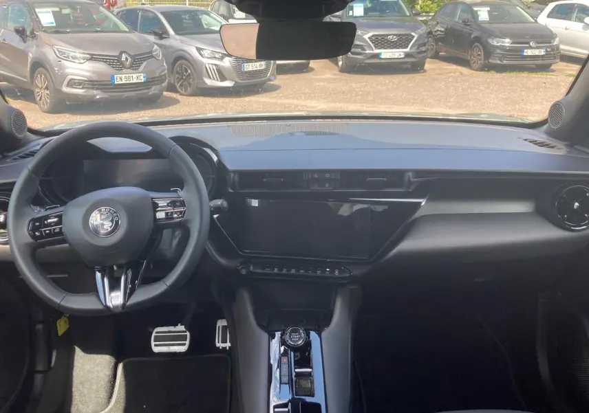 Vue intérieure avant de l'Alfa Romeo Junior 1.2 hybride 2026, tableau de bord noir avec écran tactile et volant multifonction.