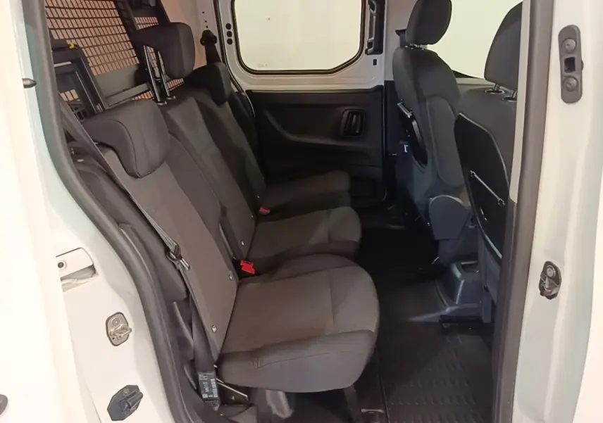 Vue intérieure côté droit sur la banquette arrière noire du Peugeot Partner blanc avec cloison grillagée visible.