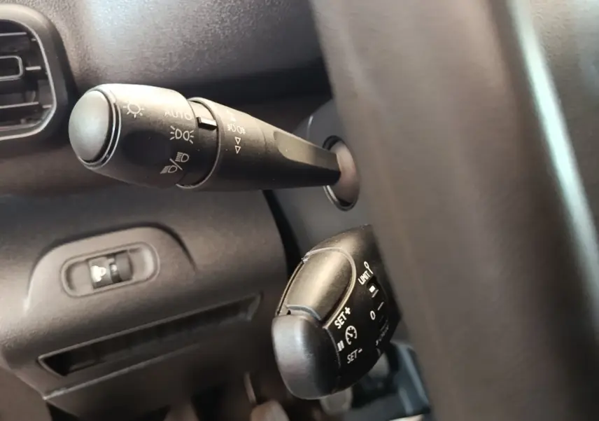 Gros plan sur les commandes de phares et régulateur de vitesse derrière le volant du Peugeot Partner blanc de 2020.