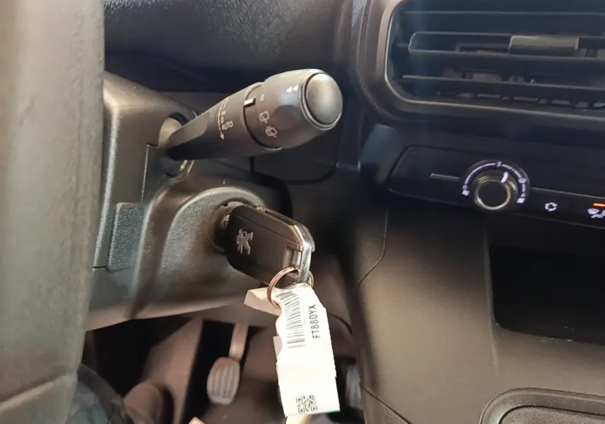 Gros plan intérieur sur le contacteur avec clé Peugeot insérée, volant et commandes noires visibles en arrière-plan.