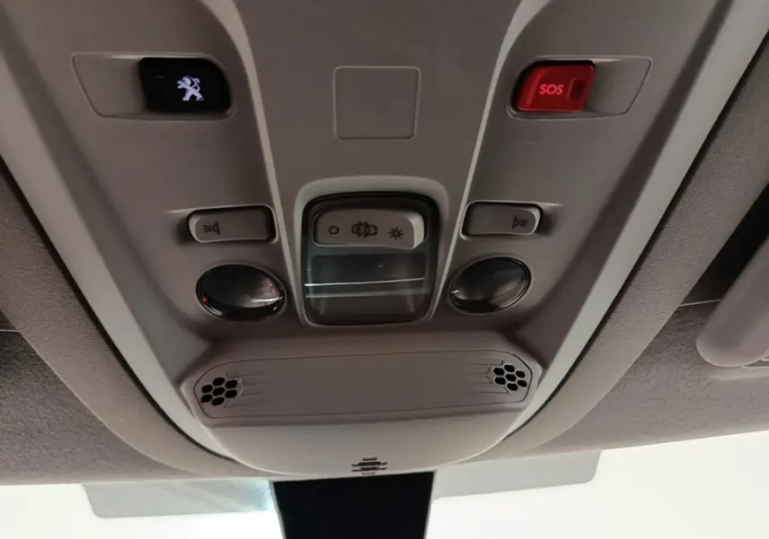 Vue en contre-plongée du panneau de commande intérieur au plafond du Peugeot Partner blanc, avec bouton SOS rouge et éclairage.
