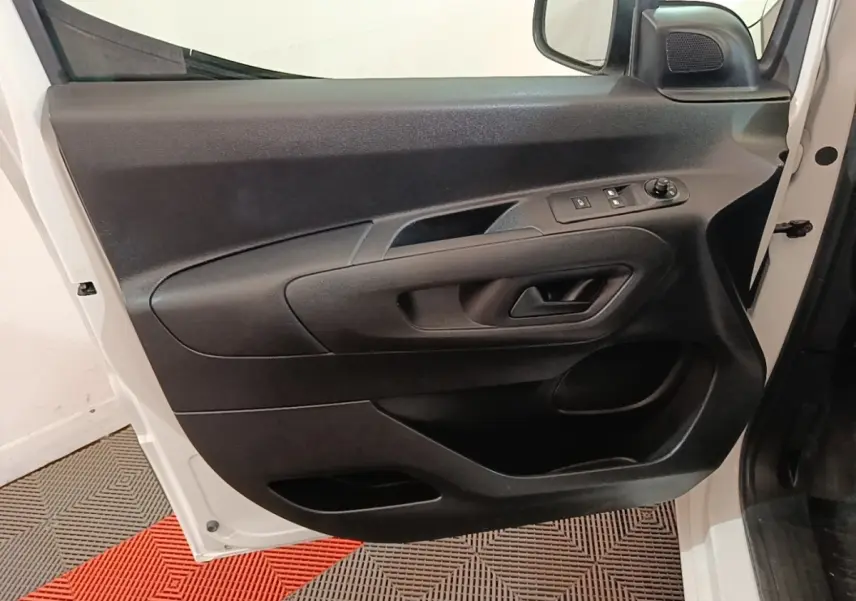 Vue rapprochée de la porte avant gauche noire à l'intérieur du Peugeot Partner blanc, avec commandes électriques des vitres.
