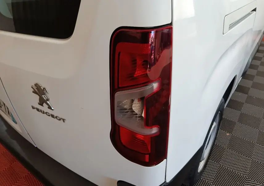 Gros plan sur le feu arrière droit d’un Peugeot Partner blanc, montrant le logo et la carrosserie arrière côté droit.